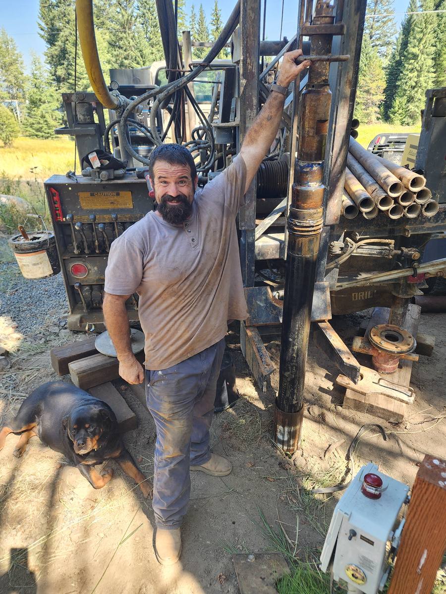 Aqua Terra crew member beside a length of stainless steel well screen pulled from a well being deepened, with drill pipe racked behind the rig